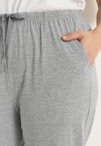 Graue elastische Hose mit einem Kordelzug, ausgestattet mit seitlichen Taschen und einem weichen, strukturierten Stoff. Einfaches Design, geeignet für die Freizeit.