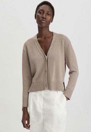Light brown knit cardigan with a deep V-neck, front buttons, ribbed hem, and side slits, paired with white trousers. Smooth texture.