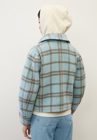 Giacca a quadri blu chiaro con una texture morbida, dotata di colletto e dettagli marroni. Il design è cropped con una vestibilità rilassata.
