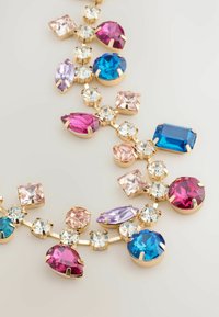 Colorful gemstone necklace featuring pink, blue, and purple crystals set in gold-tone metal. Various shapes including round, teardrop, and square.