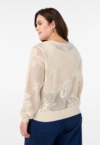 Beige stickad tröja med öppen väv, blommönster och ribbade muddar. Bakdelen har en rundad halsringning och en avslappnad passform.