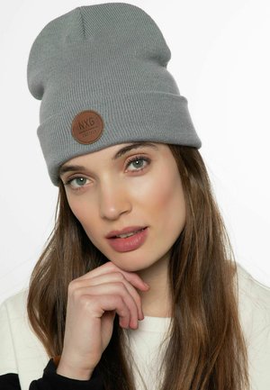 Grijze gebreide beanie gemaakt van zacht materiaal, met een opgerolde rand en een ronde bruine leren patch met "NXG PROTEST" erop geprint.