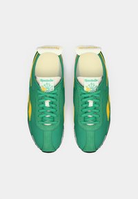 Zelena i žuta Reebok obična obuća s teksturiranim materijalom, dizajnom na vezanje, jastučićem oko vrata i logom na jeziku. Bijele potplate s crnim detaljima.