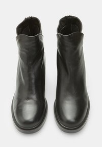 Botas de tobillo de cuero negro con una textura suave, punta redonda y diseño minimalista. Cuentan con una cremallera en la parte trasera para facilitar el uso.