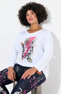 Chemise blanche à manches longues avec un graphisme coloré de tigre et le mot "AWESOME". Associée à un jean foncé avec des éclaboussures roses et des motifs de tigre.
