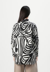 Camicia a righe bianche e nere con vestibilità ampia, maniche lunghe e colletto, caratterizzata da audaci motivi astratti su un tessuto liscio.