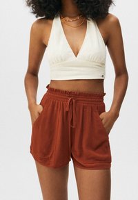 Hellcremiger Neckholder-Cropped-Top mit gerafften Details, kombiniert mit rostfarbenen, strukturierten Shorts mit elastischem Bund und Seitentaschen.