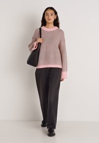 Pulover tricotat cu dungi roz și gri, mâneci largi, tiv striat, asortat cu pantaloni largi, închiși la culoare, și o geantă neagră.