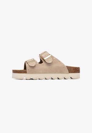 Sandalias de ante beige con dos hebillas ajustables, detalles con tachuelas, suela texturizada de corcho y goma, y diseño ondulado en la suela exterior.
