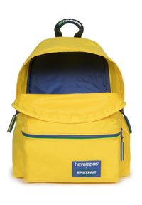 Zaino giallo con interni blu, tasca anteriore con zip e dettagli colorati. Presenta una maniglia superiore e toppe con il marchio.