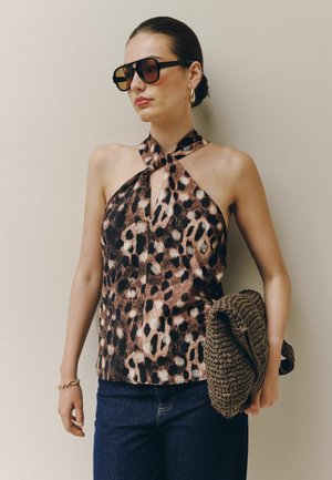 Frau trägt große Sonnenbrille, Leopardenmuster-Haltertop, blaue Jeans, goldene Creolen, hält eine geflochtene braune Clutch.