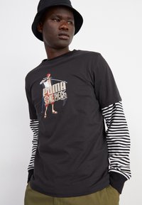 Camiseta negra con un estampado gráfico de un personaje de dibujos animados, superpuesta con mangas largas a rayas en blanco y negro, con un corte relajado.