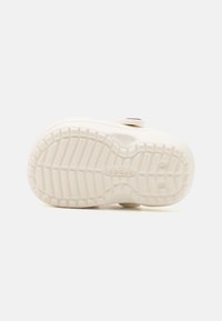 Semelle de chaussure en caoutchouc blanc avec un motif de bande de roulement texturé, une forme arrondie et un accent circulaire en haut. Nom de la marque "Crocs" visible.