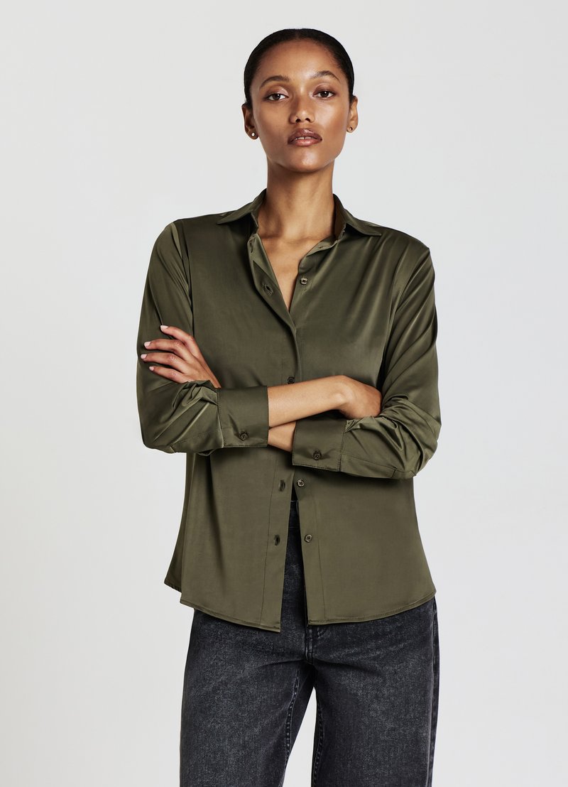 Camicia in satin verde oliva con chiusura a bottoni, colletto a punta e maniche lunghe, abbinata a jeans scuri. Tessuto liscio e vestibilità comoda.