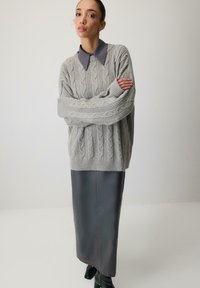 Mīksts pelēks adīts džemperis ar augstu ribotu apkakli, kombinēts ar tumšu ādas midi svārku ar redzamu šuvi.