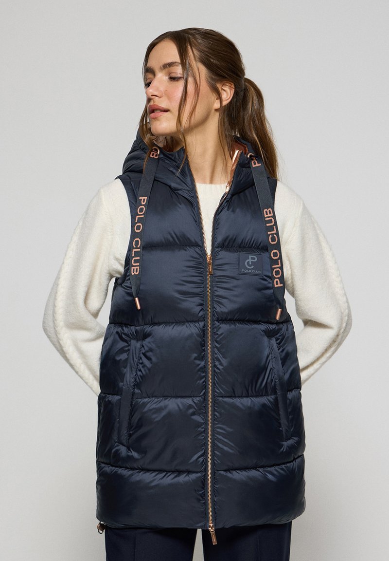 Veste sans manches matelassée bleu marine avec capuche, présentant des accents rose doré, une fermeture éclair à l'avant et deux poches latérales. Logo sur la poitrine gauche.