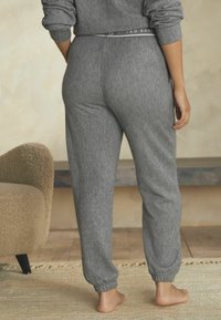 Des joggers grijs à côtes présentent une taille extensible et des poignets fuselés, complétant une coupe décontractée. Le tout se détache sur un fond neutre.