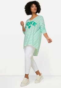 Mintgrön randig långärmad topp med "LOVE"-grafik, matchad med vita smala byxor och ljusa sneakers, med en rundad nederkant.