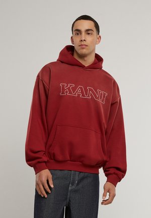 Rote Kapuzenjacke mit einem großen "KANI"-Logo in kontrastierendem Stich, ausgestattet mit einer Fronttasche, gerippten Bündchen und einem lässigen, übergroßen Schnitt.