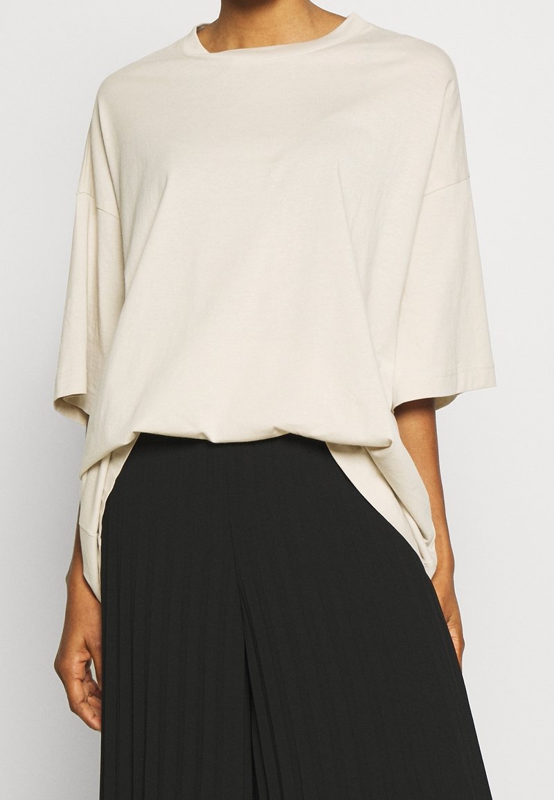 Licht beige oversized t-shirt van zachte katoen, met brede mouwen en een relaxte pasvorm, gecombineerd met een zwarte plissérok.