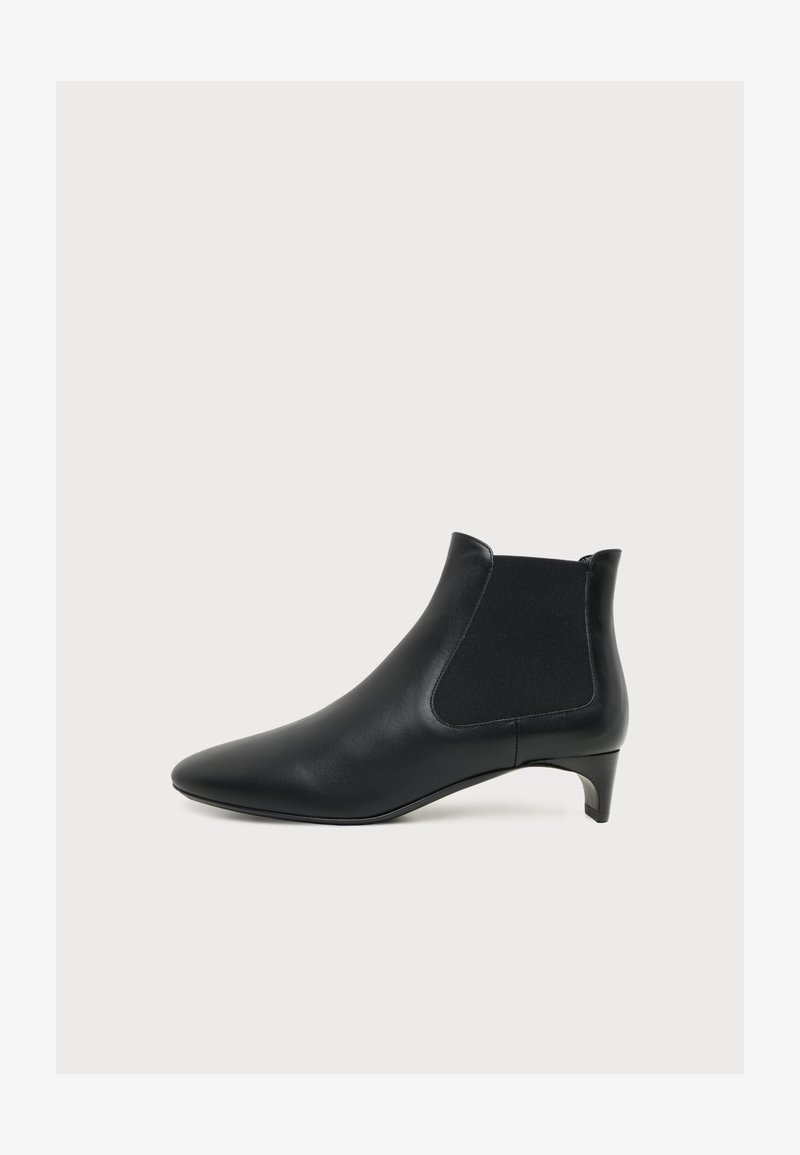 Bottine en cuir noir avec bout pointu, panneau latéral élastique et petit talon kitten sur fond clair uni.