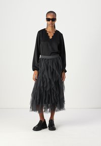 Črna satenska bluza s scalloped ovratnikom, v kombinaciji z večplastno, naborkano črno tila krilo. Model nosi črne platform čevlje in sončna očala.