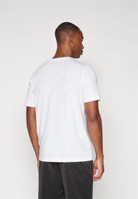 Witte t-shirt met korte mouwen, ronde halslijn, zachte katoenen stof, relaxed fit. Draagt een model, gezien van achteren.