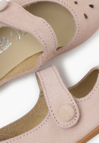 Jasnoróżowe zamszowe buty dziecięce z zaokrąglonym noskiem, wycięciami, rzepem i brązową podeszwą. Miękka tekstura i prosty design.