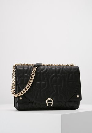 Sort skuldertaske i læder med abstrakt prægning, guldkæde og guldlås, vist på en hvid podium mod en ensfarvet baggrund.