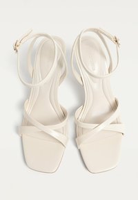 Sandales à talons hauts beige avec un bout carré, en cuir lisse, dotées de brides croisées et d'une sangle à la cheville pour la fermeture.