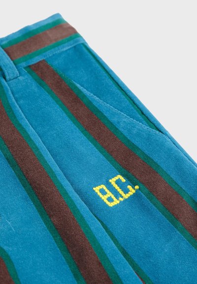 Baršunaste plave hlače s zelenim i smeškim prugama, sa žutim izvezenim natpisom "B.C." na prednjem džepu. Mekana tekstura i kroj prilagođen figuri.