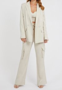 Beige bleiseri, joka on räätälöity kahdella etutaskulla ja hopeisilla yksityiskohdilla, päällä yhteensopiva crop-top ja leveälahkeiset cargo-housut, joissa on sivutaskut.