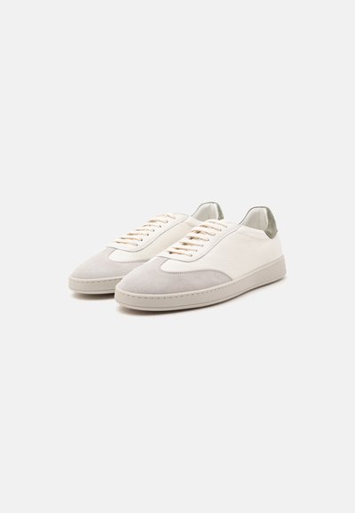 Paire de baskets basses blanches avec bouts en daim gris clair et détails gris au talon, lacets beige et semelles plates en caoutchouc sur fond blanc.