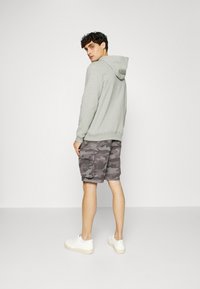 Gray hooded sweatshirt with long sleeves paired with camo-patterned cargo shorts. Model wears white sneakers. Simple and casual outfit.
