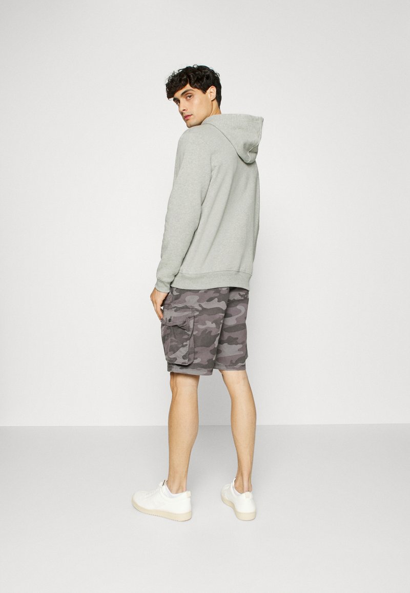 Sweatshirt à capuche gris avec manches longues, associé à un short cargo à motif camouflage. Le mannequin porte des baskets blanches. Tenue simple et décontractée.