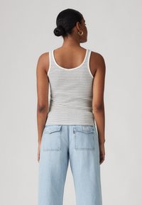 Canottiera a righe in bianco e grigio, realizzata in tessuto a coste, abbinata a jeans di denim chiari e larghi con due tasche posteriori.