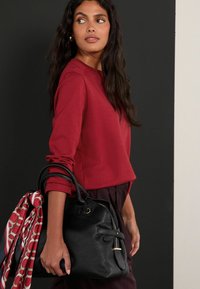 Piros hosszú ujjú felső, fekete bőr táskával párosítva, a táska fülére kötve piros és fehér mintás sál. Simább textúra, laza stílus.