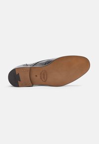 Suola di scarpa in pelle nera con una finitura marrone liscia, caratterizzata da un motivo di piccole perforazioni, dettagli metallici e marchi.