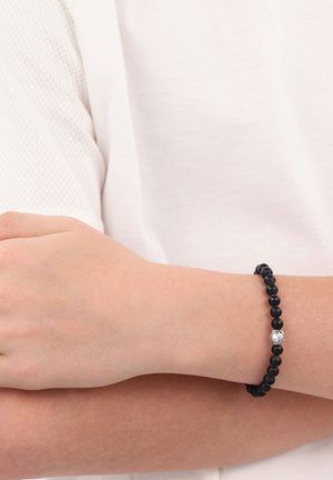 Schwarzes Perlenarmband aus glatten, runden Steinen, mit einer silbernen Akzentperle im Marmorierungsmuster, getragen am Handgelenk.