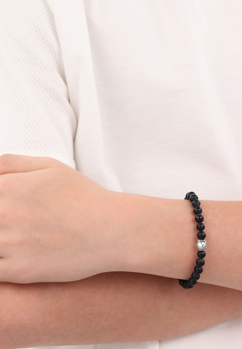 Bracciale di perle nere realizzato con pietre lisce e rotonde, dotato di una perla di accento argentata con un motivo marmorizzato, indossato su un polso.