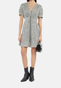 Sukienka w panterkę w odcieniach czerni i bieli, z krótkimi bufkami, dekoltem w kształcie litery V i z przodu na guziki. W zestawie z czarną torbą i botkami za kostkę.