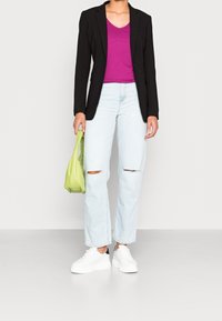 Svart blazer, fuchsia topp med v-ringning, ljusblå ripped jeans och vita platåskor. Håller en liten grön handväska.