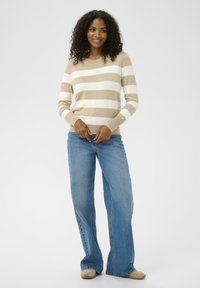 Beige og hvide stribede trøje med lange ærmer, kombineret med lyseblå jeans med vide ben og beige sko. Glat tekstur.