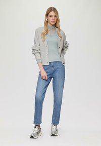 Grijze gebreide cardigan, lichtblauw topje, blauwe jeans en zilveren sneakers. Cardigan heeft knopen en geribde manchet; top heeft een kanten patroon.