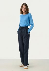 Maglione azzurro chiaro a maniche lunghe abbinato a pantaloni scuri in tessuto elasticizzato con vita elasticizzata. L'outfit presenta una vestibilità comoda e tasche laterali. Sneakers casual.