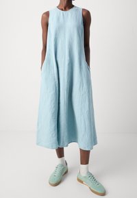 Vaaleansininen pellavaseosmekko, jossa on hihaton malli, sivutaskut ja lentävä siluetti, yhdistettynä mintunvihreisiin tennareihin ja valkoisiin sukkiin.