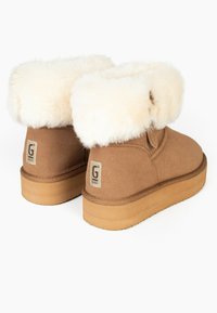 Botas de tobillo de ante color tan con un puño de piel de crema esponjosa y una suela de goma beige. Parche con el logo visible en la parte trasera cerca del talón.