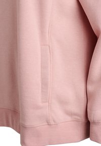 Růžová mikina s měkkou texturou, vybavená boční kapsou a žebrovanými manžetami. Jsou viditelné švy podél rukávů a lemu.