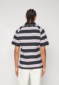 Schwarz- och rosa randig polo skjorta med korta ärmar, krage och avslappnad passform, i kombination med ljusa byxor.