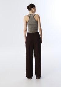 Top grigio senza maniche con un design aderente e una texture a coste, abbinato a pantaloni larghi a gamba larga di un borgogna scuro.